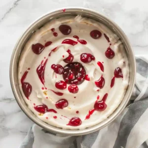 Top view of raspberry preserves being swirled into bundt cake batter inside a bundt pan