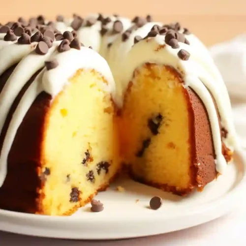 Vertical photo of a slice of Nothing Bundt Cake Vanilla with chocolate chips and frosting on a plate